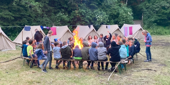 Kinder sitzen um ein Lagerfeuer herum