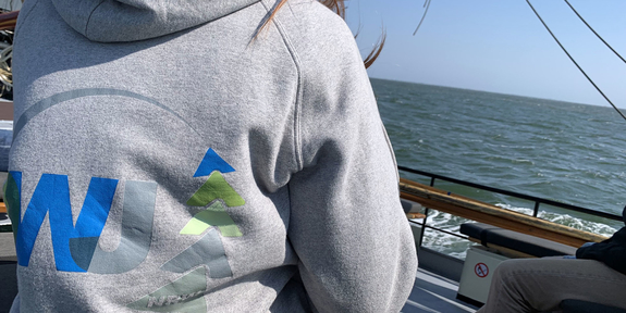 DWJ Logo auf Pullover, Person sitzt auf einem Segelschiff